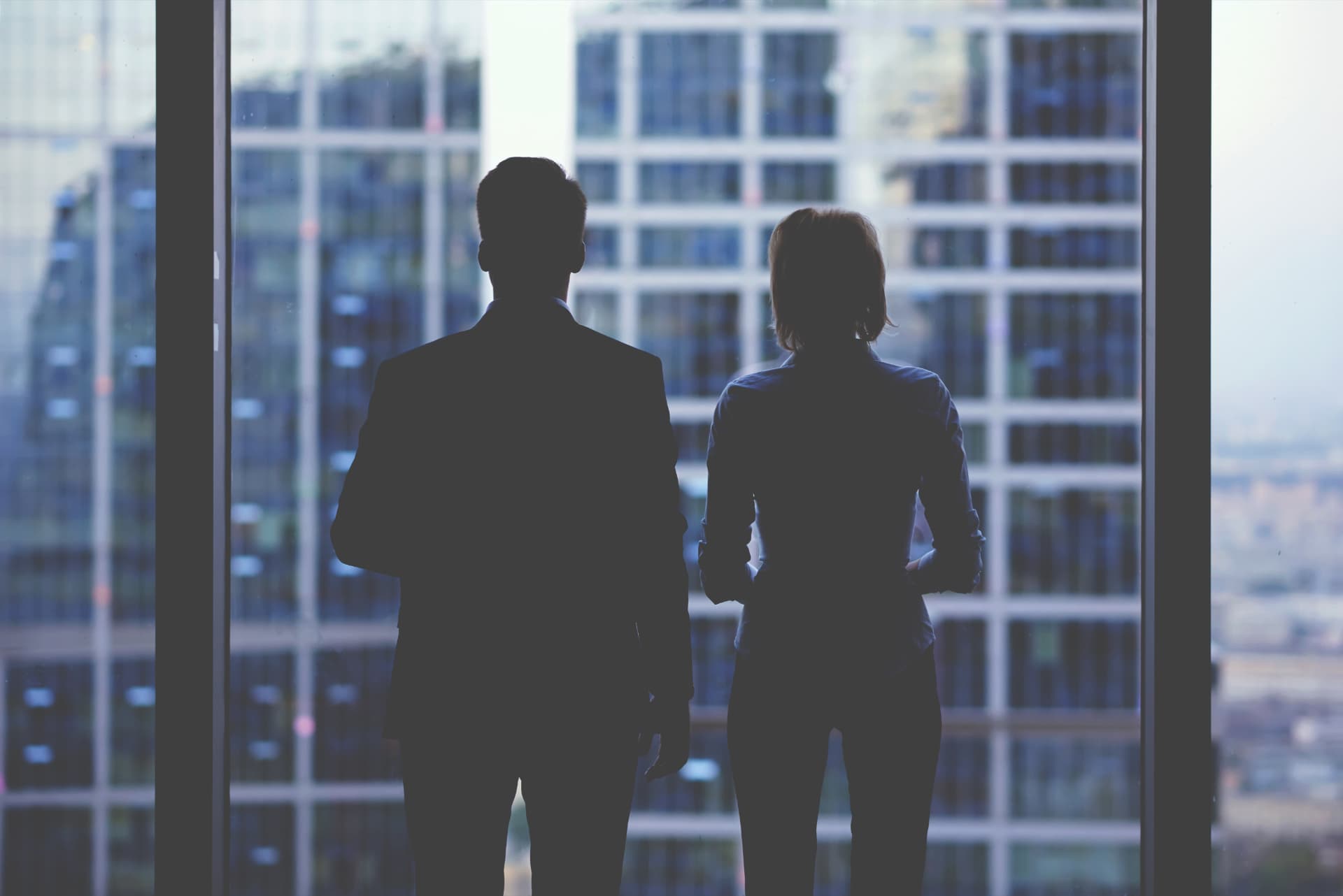 Due figure professionali in silhouette davanti a una vetrata di grattacieli, metafora della governance aziendale